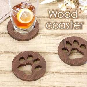 May include: Wooden coasters with a paw print design. One coaster holds a glass of iced tea with a lemon slice. The coasters are dark brown and round, with the text "Wood coaster" in the background.