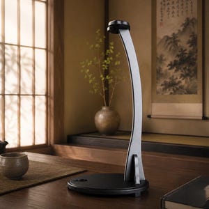 May include: A tall, curved silver-toned stand with a black circular base. The stand features a smooth, elongated vertical arm that arches upward, terminating in a small, rounded top piece designed for supporting an object, set on a flat surface.