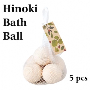 Op de afbeelding: Een set van vijf lichtgekleurde Hinoki houten badballen in een wit netzakje met trekkoord. Een rechthoekig kartonnen label met een botanische print van groene bladeren en rode bessen is aan het zakje bevestigd. De tekst "Hinoki Bath Ball" en "5 pcs" is in het zwart op de afbeelding gedrukt.