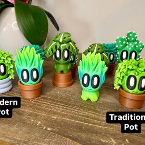 K&ouml;nnte beinhalten: Acht kleine gr&uuml;ne und blaue Pflanzenfiguren mit verschiedenen Gesichtsausdr&uuml;cken und Topfformen. Einige T&ouml;pfe sind modern und andere traditionell.