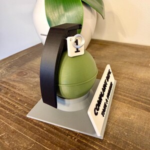 May include: A novelty desk ornament shaped like a green grenade with a black handle and a white tag with the number 1. A white sign reads "COMPLAINT DEPT. TAKE A NUMBER."