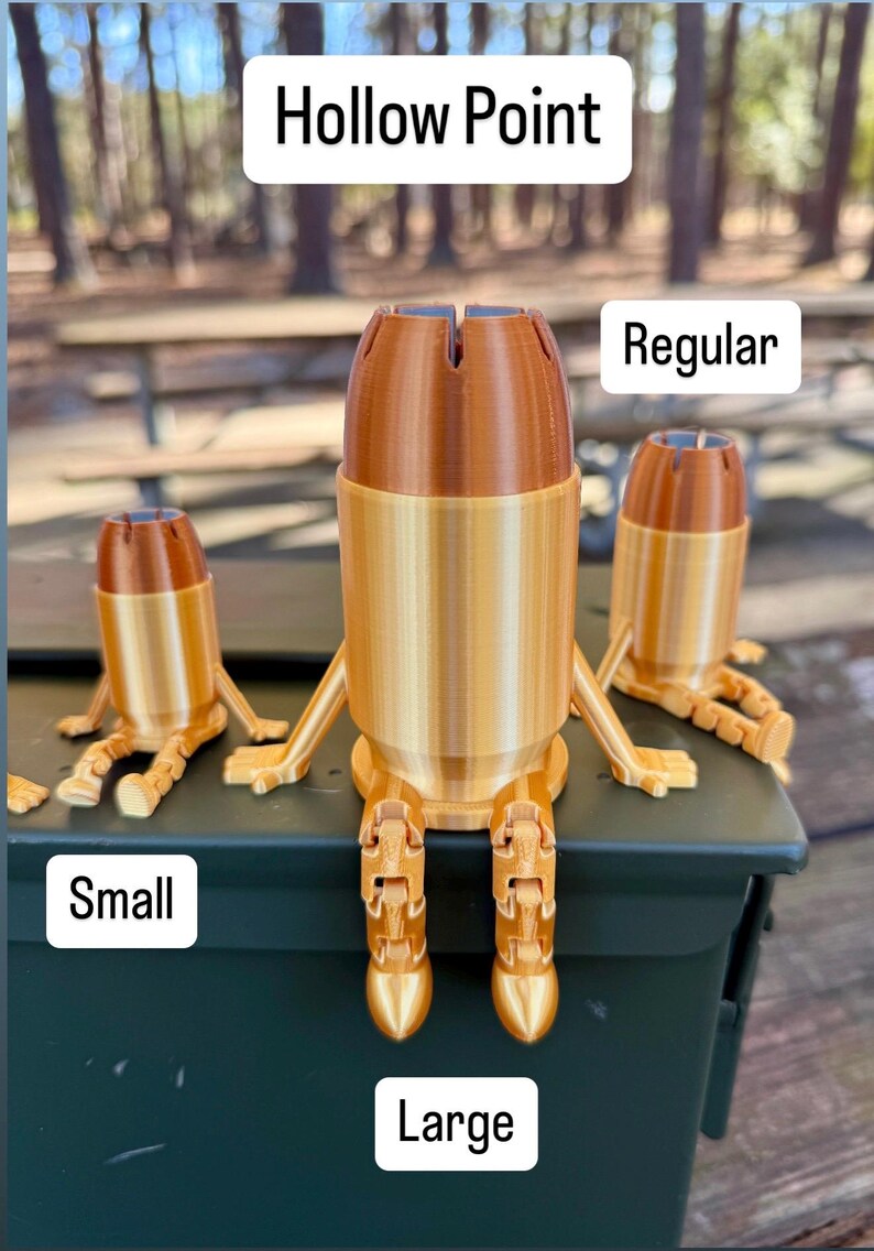 May include: Three 3D printed bullet-shaped figurines with legs. The figurines are sitting on a green box. The largest figurine is labelled "Large", the middle figurine is labelled "Regular", and the smallest figurine is labelled "Small". The top of the largest figurine is labelled "Hollow Point".