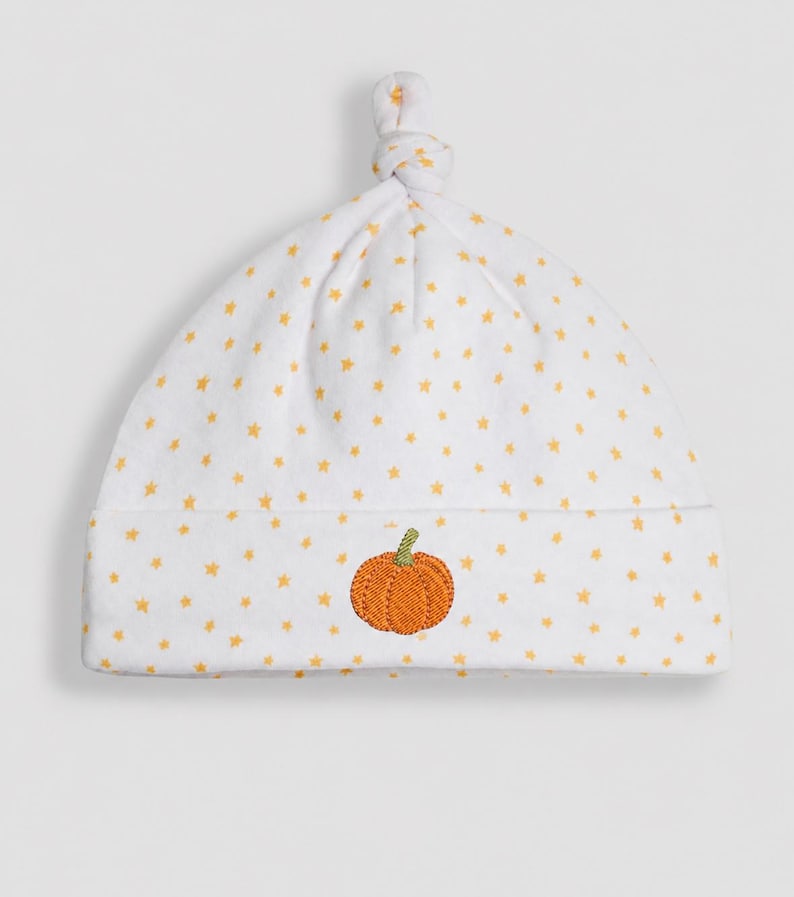 May include: A white baby hat featuring a pattern of small yellow stars and a knotted top. The front of the hat is embroidered with a single orange pumpkin with a green stem centred on the folded brim, providing a simple and clear design.
