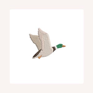 May include: An embroidered patch featuring a mallard duck in flight. The duck has a green head, white and gray wings, and a brown body. The patch is set against a white background.