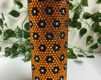 May include: A stainless steel tumbler adorned with orange, black, and silver rhinestones. The design showcases a pattern of orange rhinestones with black and silver accents. The tumbler has a silver lid and is designed to keep drinks cold or hot.