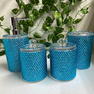 May include: Set of four turquoise blue bathroom containers with clear lids and a matching turquoise blue soap dispenser. The containers are covered in small, sparkly rhinestones.