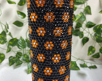 May include: A stainless steel travel mug, embellished with black rhinestones and orange and silver floral patterns. The mug has a silver lid. A decorative and functional item, designed to keep drinks hot or cold.