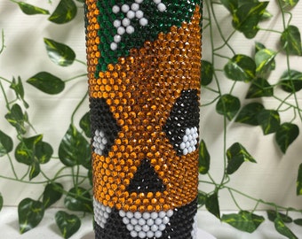 May include: A stainless steel tumbler decorated with orange, green, black, and white rhinestones. The design features a green section with a white cross, an orange section, and a black section with white accents. The tumbler is cylindrical.