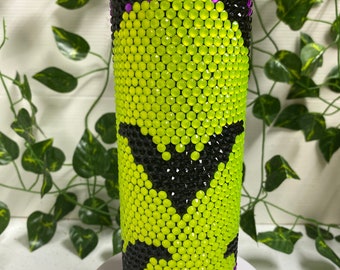 May include: A stainless steel tumbler decorated with lime green, black, and purple rhinestones. The design features a bat silhouette. The top and bottom rims are lined with purple rhinestones. The tumbler is cylindrical and has a silver lid.