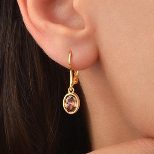May include: Gold dangle earrings with a round, light brown gemstone.