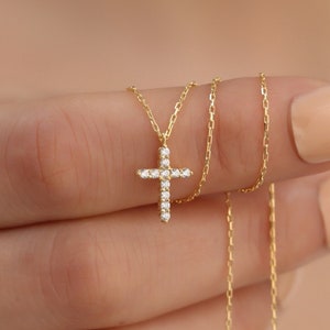 May include: A delicate gold chain necklace with a small, sparkling diamond cross pendant.