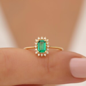 May include: A gold ring with a green emerald gemstone surrounded by a halo of small diamonds.