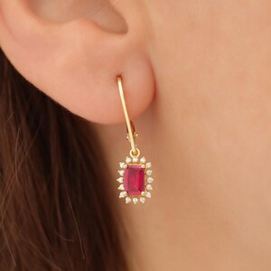 May include: Gold dangle earrings with a red gemstone surrounded by smaller clear gemstones.