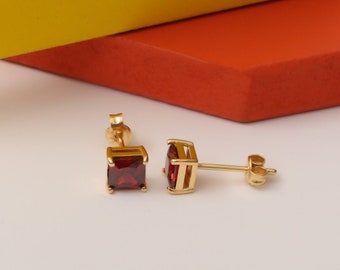 May include: A pair of gold stud earrings with square red gemstones.