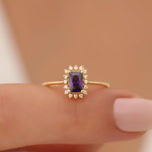 May include: A gold ring with a purple gemstone surrounded by smaller clear gemstones.