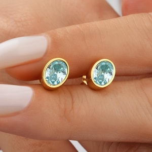 May include: A pair of gold stud earrings with oval-shaped light blue gemstones.