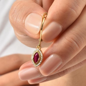 Könnte beinhalten: Ein goldener Ohrhänger mit einem roten, markisenförmigen Edelstein, der von einem Heiligenschein aus kleineren, klaren Edelsteinen umgeben ist.