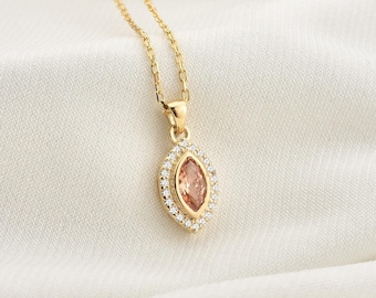 May include: A gold necklace with a pendant featuring a marquise-shaped pink gemstone surrounded by a halo of smaller clear gemstones.