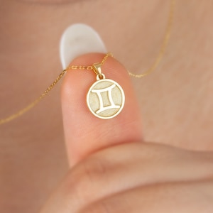 May include: Gold necklace with a round pendant featuring the Gemini zodiac symbol.
