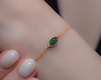 May include: A delicate gold chain bracelet featuring a single marquise-shaped green gemstone.