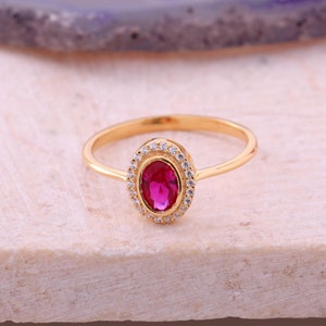 May include: A gold ring with a red oval gemstone surrounded by a halo of smaller white gemstones.