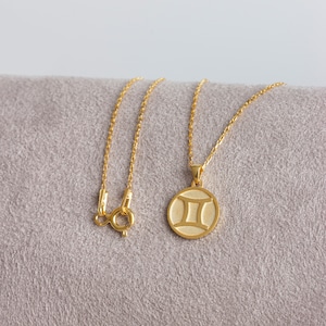 May include: A gold chain necklace with a round pendant featuring the Gemini zodiac symbol.