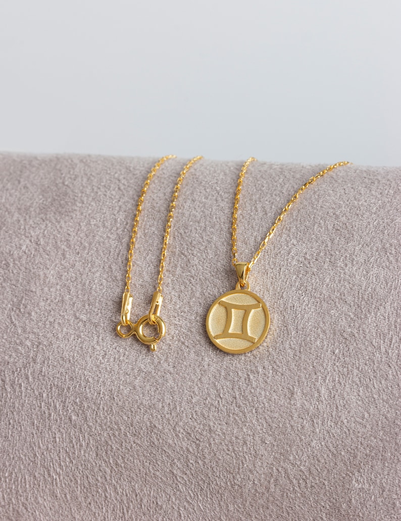 May include: A gold chain necklace with a round pendant featuring the Gemini zodiac symbol.