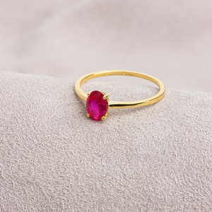 May include: A gold ring with a bright pink oval-shaped gemstone.