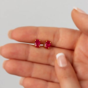 May include: A pair of gold stud earrings with oval-shaped red gemstones.