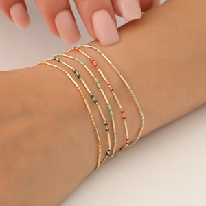 Peut inclure: Un ensemble de six bracelets en or avec des perles en émail coloré. Chaque bracelet présente une couleur différente de perles en émail, notamment rouge, orange, turquoise et vert.