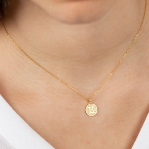 May include: A gold chain necklace with a small, round pendant featuring the Gemini zodiac symbol.