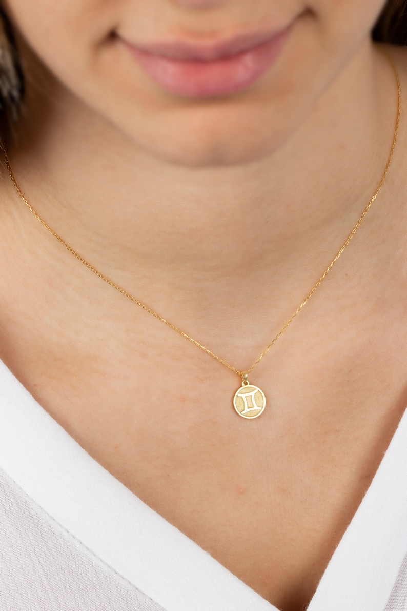 May include: A gold chain necklace with a small, round pendant featuring the Gemini zodiac symbol.