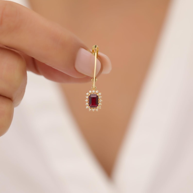 May include: Gold dangle earring with a red gemstone surrounded by small white gemstones.