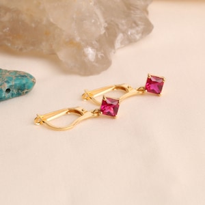 May include: A pair of gold earrings with a dangling square-shaped pink gemstone.