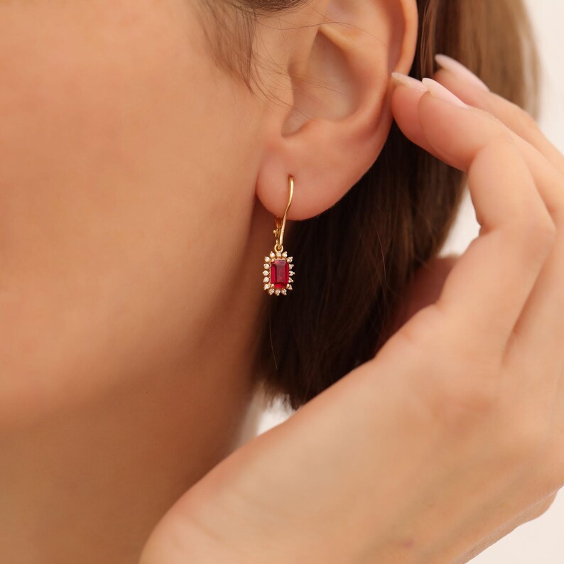 May include: Gold dangle earrings with a red gemstone surrounded by smaller clear gemstones.