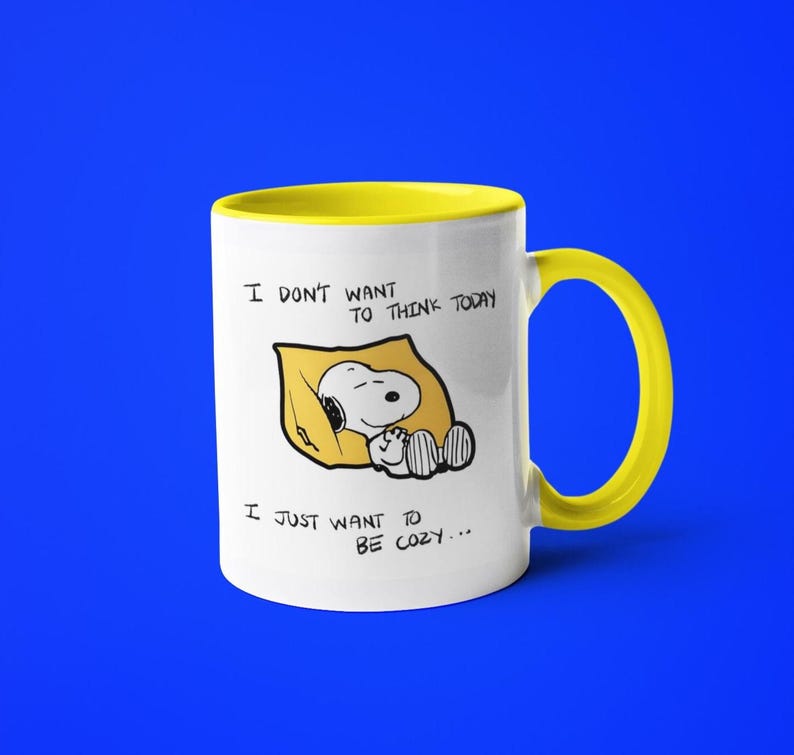 May include: White ceramic mug with a yellow interior and handle. The mug features a cartoon Snoopy character sleeping on a yellow pillow, with the text "I DON'T WANT TO THINK TODAY, I JUST WANT TO BE COZY..." printed on the front.