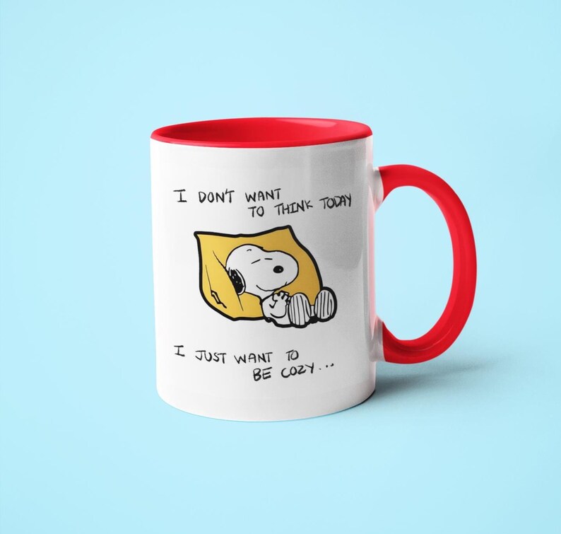 May include: White ceramic mug with a red interior and handle. The mug features a Snoopy illustration in a yellow blanket with the text "I DON'T WANT TO THINK TODAY, I JUST WANT TO BE COZY..."