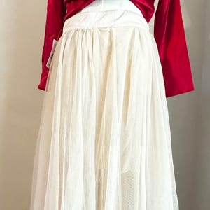 May include: A formal gown featuring a red satin top and a layered, flowing skirt. The skirt is made of sheer, off-white fabric with delicate edging. The gown's design suggests a vintage or romantic aesthetic, suitable for special occasions.