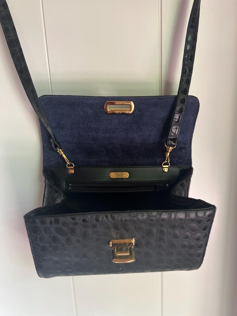 May include: Black crocodile embossed leather crossbody bag with a gold clasp and a blue suede lining. The bag has a small pocket on the inside and a long strap.