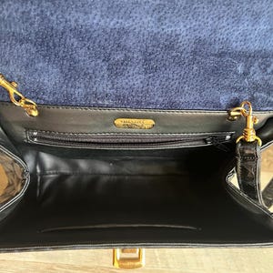 May include: Black leather handbag with a gold chain strap and a gold clasp. The bag has a blue suede lining and a label that reads "Valentino."