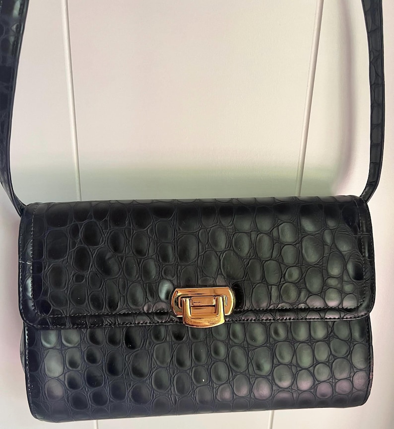 May include: A black crocodile embossed leather shoulder bag with a gold clasp closure.