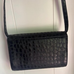 May include: A black crocodile-embossed leather shoulder bag with a flap closure.