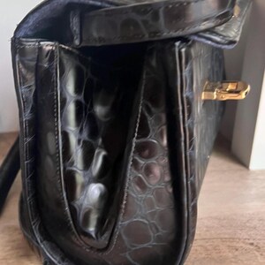 May include: Black leather handbag with a crocodile embossed pattern and a gold clasp.