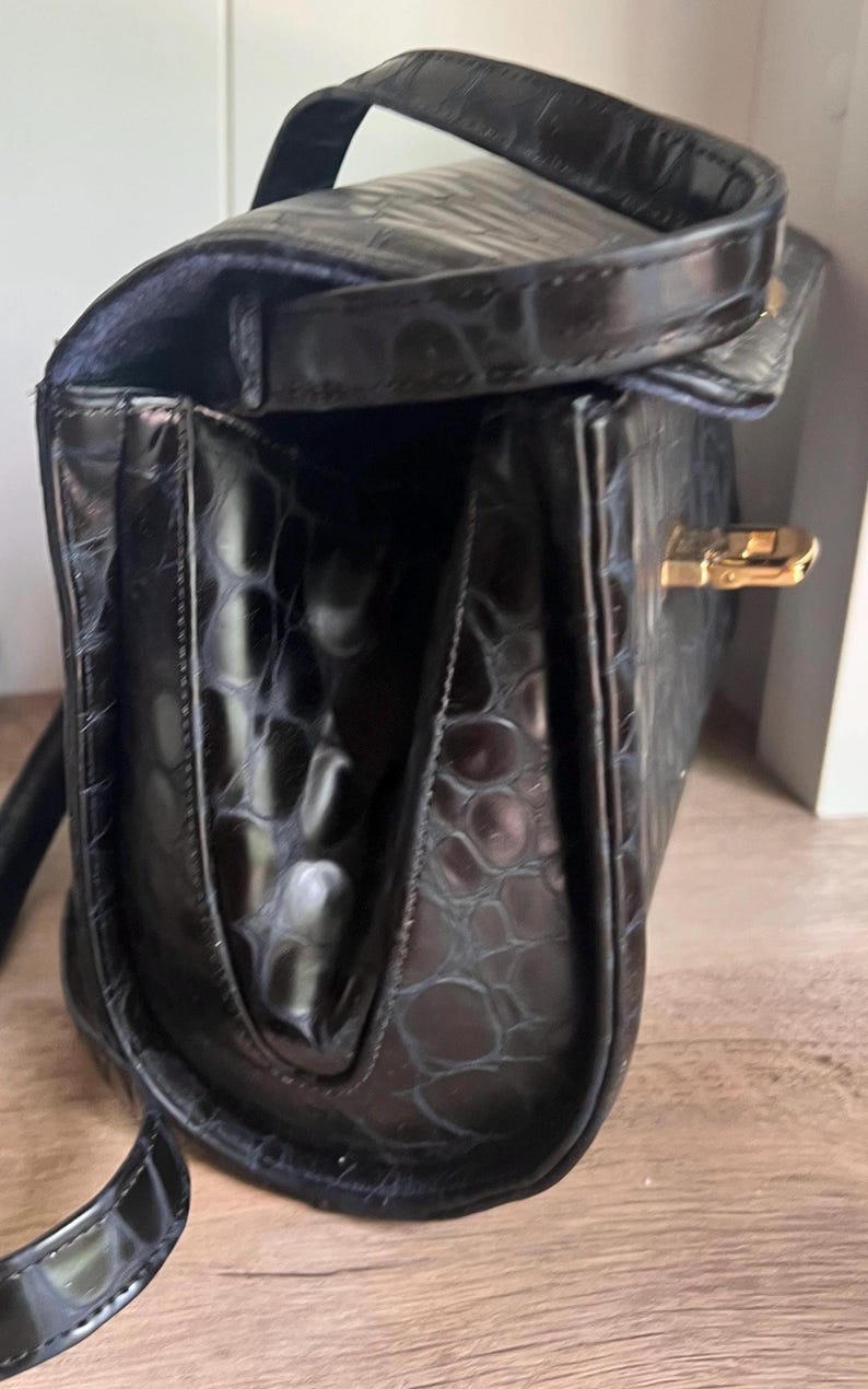 May include: Black leather handbag with a crocodile embossed pattern and a gold clasp.