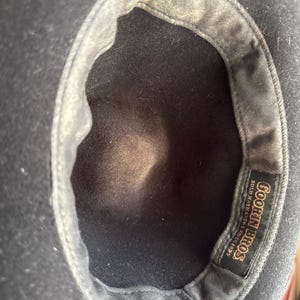 May include: A black hat viewed from the interior, featuring a dark fabric lining and a rectangular black label stitched into the inner band. The label displays the gold text Goorin Bros. Bold Hatmakers Since 1895 in a decorative serif font.