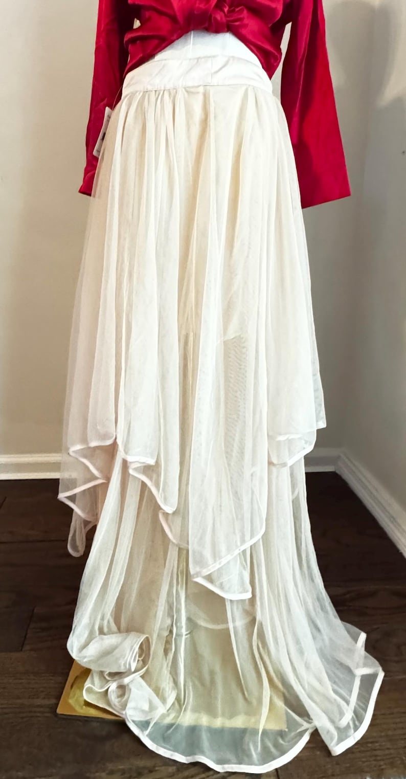 May include: A formal gown featuring a red satin top and a layered, flowing skirt. The skirt is made of sheer, off-white fabric with delicate edging. The gown's design suggests a vintage or romantic aesthetic, suitable for special occasions.