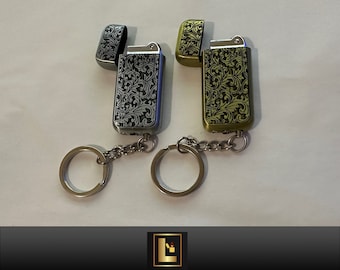 Puede incluir: Dos llaveros plateados y dorados con encendedores. Los encendedores tienen un patrón floral y están unidos a una cadena plateada y un llavero plateado.