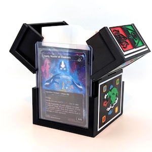 Könnte beinhalten: Schwarze, dreiteilige Kartenaufbewahrungsbox mit Klappdeckeln. Die Box enthält eine Karte mit dem Text "Aang, Master of Elements". Die Box hat farbenfrohe grafische Designs auf den Deckeln. Die Box ist für Sammelkarten konzipiert.