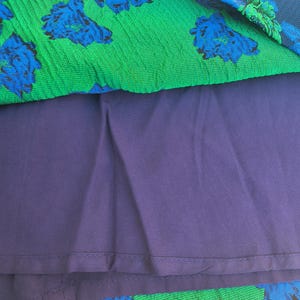 May include: A close-up of a dress with a layered design. The top layer is green with a blue floral pattern. The middle layer is a solid dark purple. The bottom layer is a dark purple floral pattern.