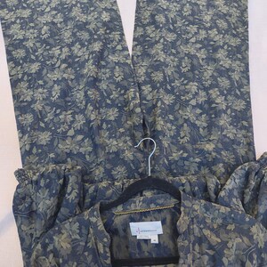 May include: A two-piece floral print outfit in shades of blue and green. The set includes wide-leg pants and a button-down shirt. The shirt is hanging on a black hanger. The fabric has a delicate floral pattern.
